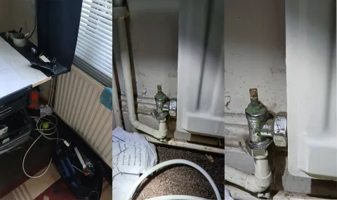 Seized radiator bleed valve at point of catastrophic failure. The valve mechanism is visibly corroded and immobile, preventing isolation of the water supply and causing uncontrolled discharge. This constitutes a direct breach of landlord repair and safety duties. Legal paperwork is visible beneath the valve, demonstrating secondary consequential harm arising from the initial mechanical failure.